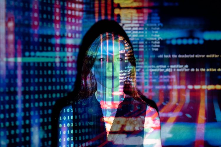 A woman standing in front of a wall with multiple strings of computer code being projected onto her