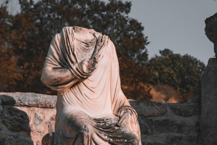 A headless statue set against a backdrop of trees and a stone wall.