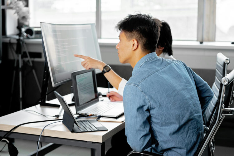 Two developers looking at lines of code on a monitor